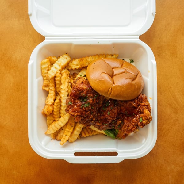 Spicy fried chicken sandwich and crinkle-cut fries in a white takeout container.