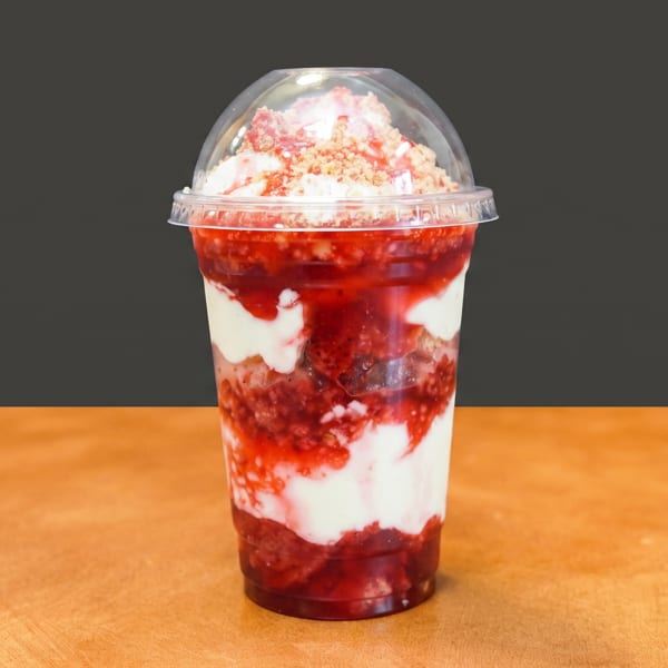 Strawberry and cream parfait in a clear cup with crumbly topping on a wooden surface.